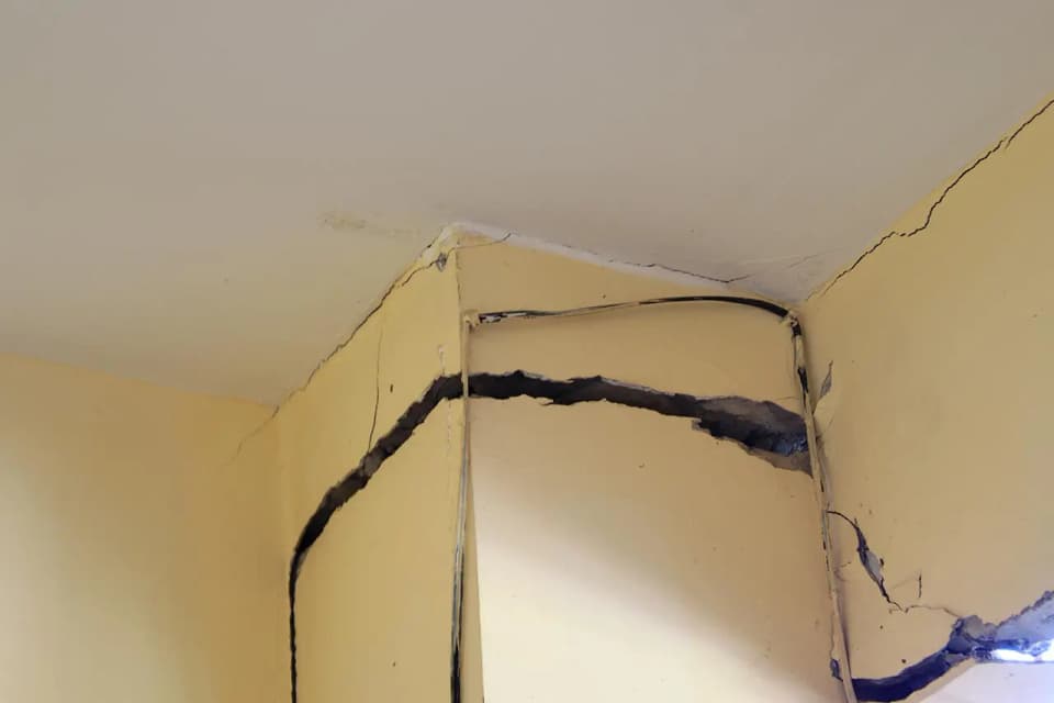 Wide cracks splitting the drywall around an interior corner just below the ceiling
