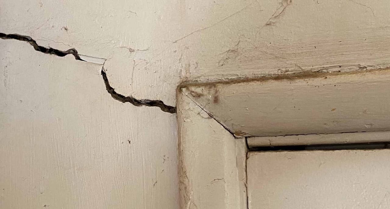 Drywall crack spreading diagonally from the top corner of an interior door frame
