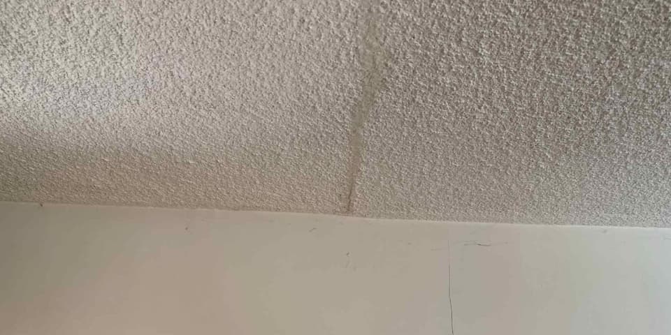 Settlement crack running across a textured ceiling and down into the wall junction