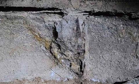 Close view of a concrete surface where the face has flaked and broken away, exposing the stone aggregate inside