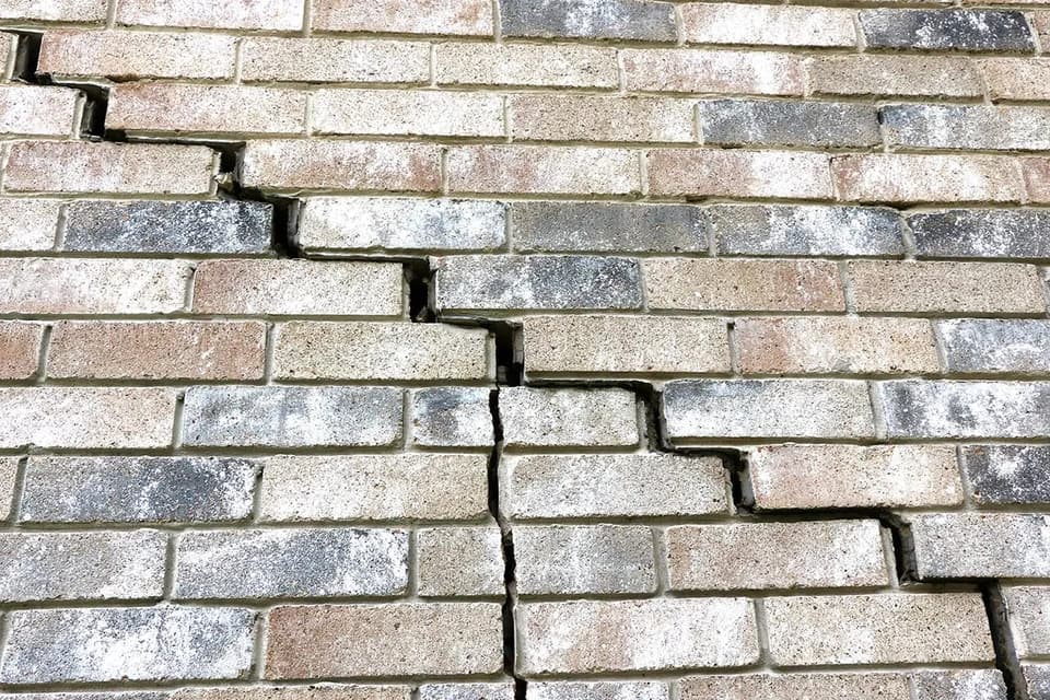 Stair step crack running through the mortar joints of a lichen stained brick veneer wall