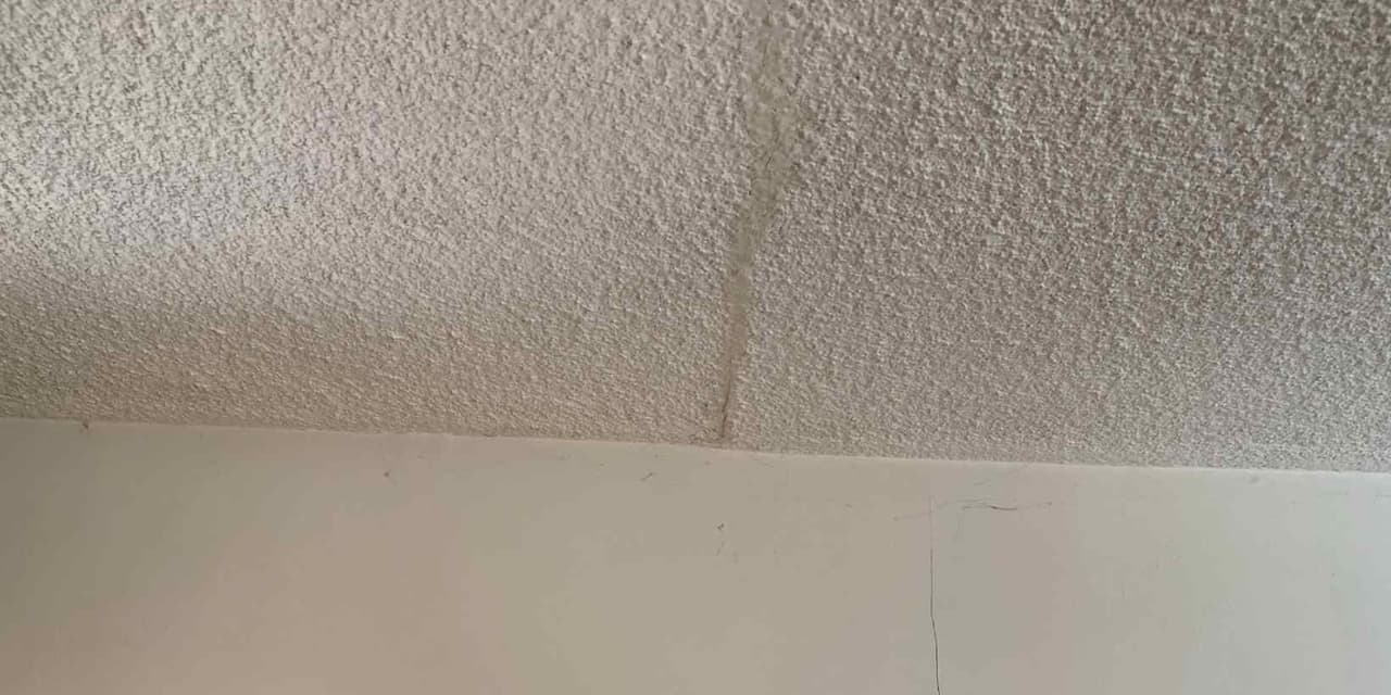 Crack running down a textured ceiling toward the joint where it meets the wall