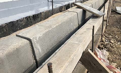 Freshly poured concrete footing inside wooden forms, with steel rods rising from the soil beside it
