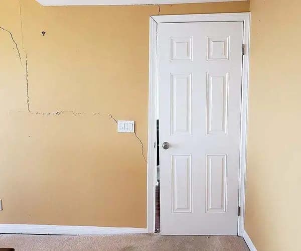 Cracks spreading across an interior wall beside a door frame in a settling home
