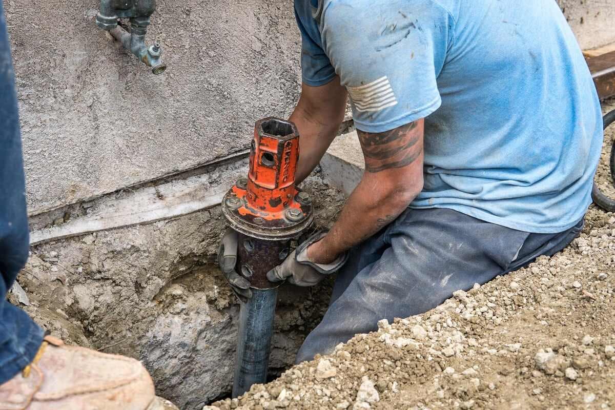 Technician guiding a push pier section into the drive head at the footing of a stucco home