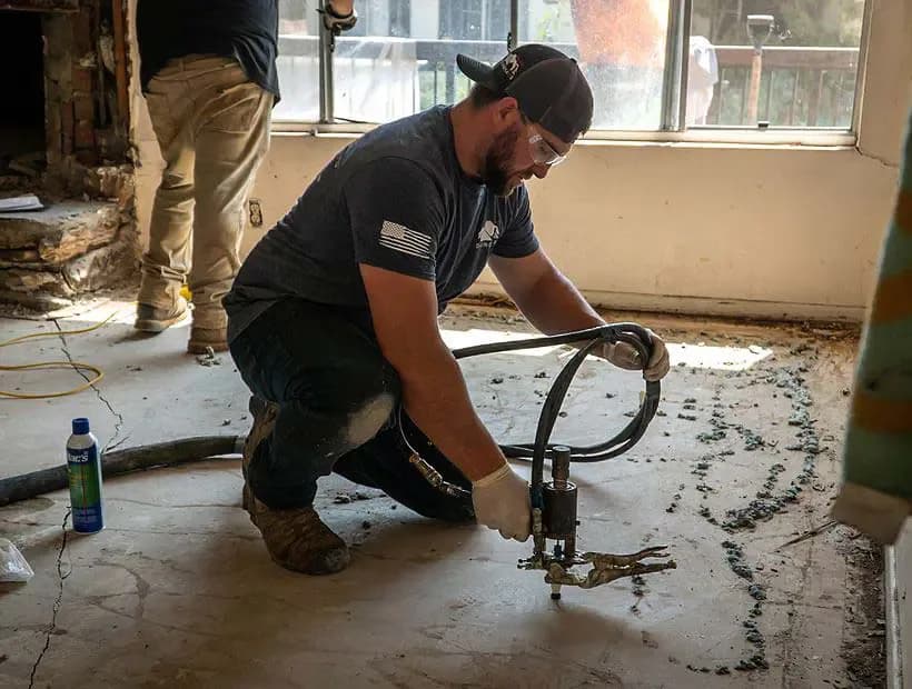 Technician injecting polyurethane through a port in a concrete floor to lift the slab back to level