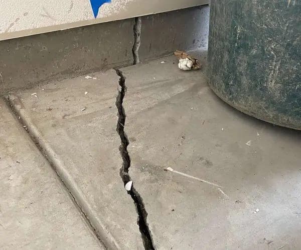 Wide crack running across a concrete garage floor beside a storage drum