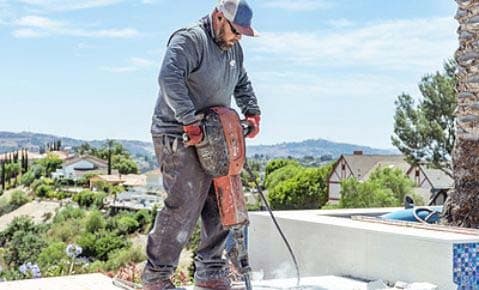 Crew member breaking up a pool deck with a jackhammer on a hillside property