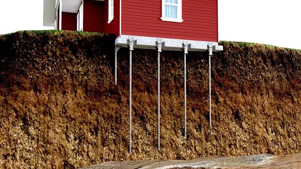 Cutaway render of a house carried on steel piers driven down through the soil to firm ground