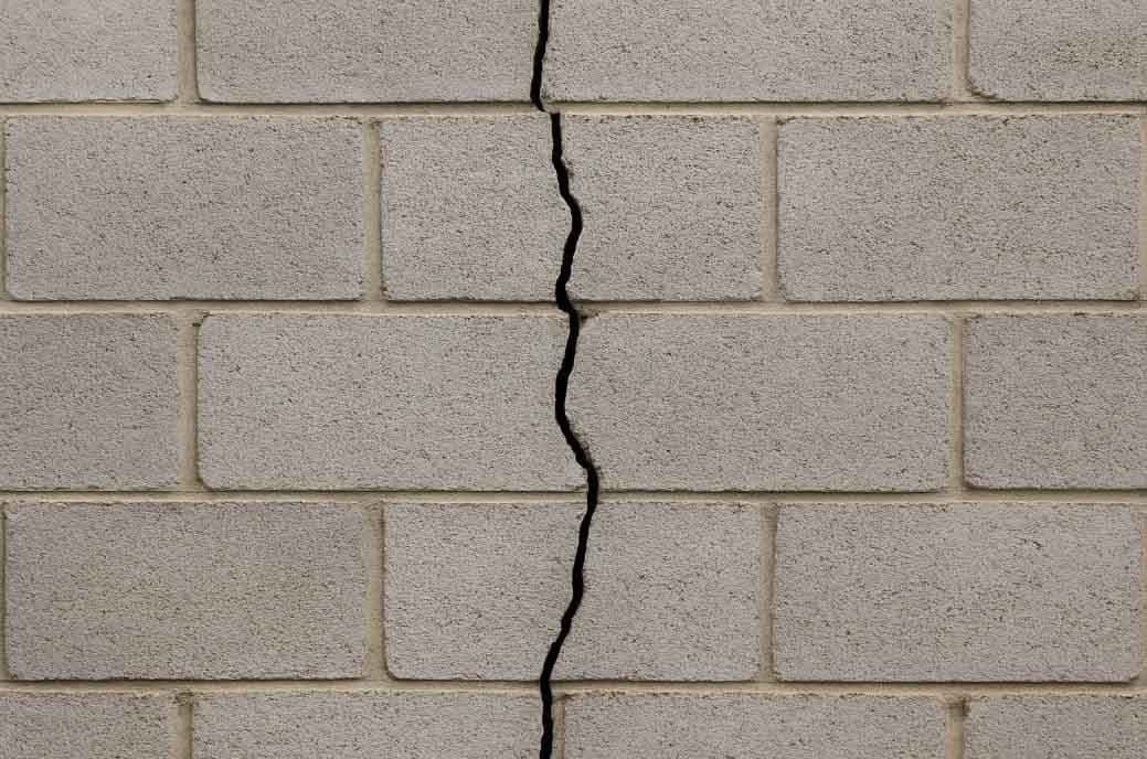 Vertical crack running straight down through the courses of a cinder block wall