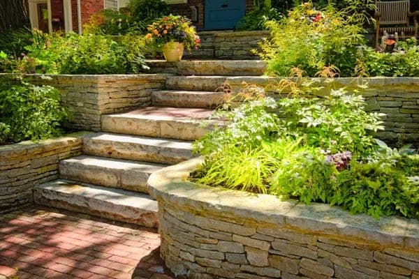 Tiered stone retaining walls holding a planted garden slope beside a set of steps