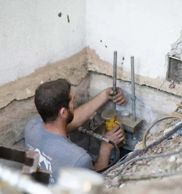 Technician working in an excavated pit against a concrete foundation wall