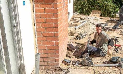 Crew member installing a pier bracket in an excavation at the base of a brick chimney
