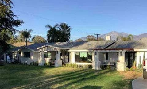 Single story ranch home with a green lawn, palm trees and mountains behind it