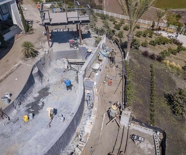 Aerial view of a hillside property under slope stabilization work, with equipment set along the graded bank