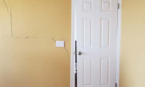 Cracks spreading across a yellow interior wall beside a white door