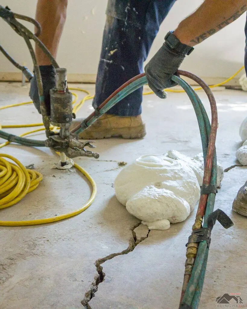 Worker injecting polyurethane foam through a cracked concrete slab, with expanded foam rising beside the crack