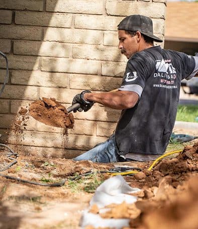 Dalinghaus crew member shoveling soil out of a trench beside a block wall