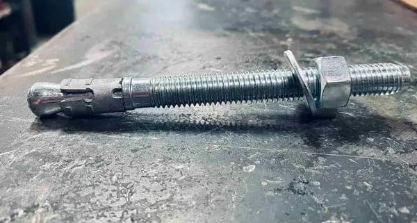 Close view of a threaded wedge anchor resting on a concrete surface