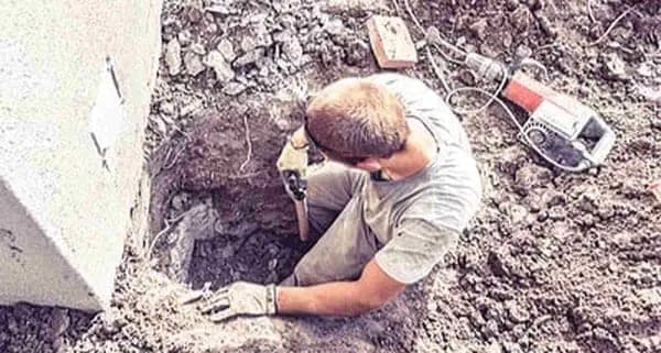 Helical pier being turned into the ground beside a house footing during underpinning