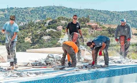 Five crew members breaking up a pool deck with jackhammers on a hillside