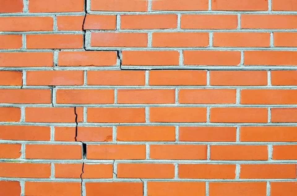Stair step crack running through the mortar joints of an orange brick wall
