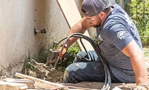 Crew member working hydraulic equipment at the base of a stucco wall