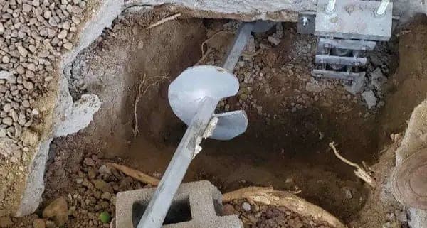 Helical pier being turned into the soil in an excavated pit beside a foundation
