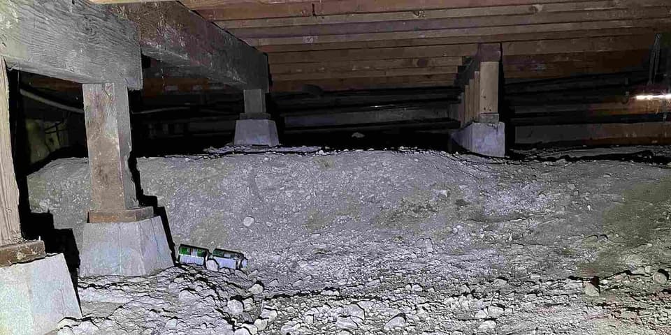 Crawl space wood support posts standing on concrete pier pads over bare dirt