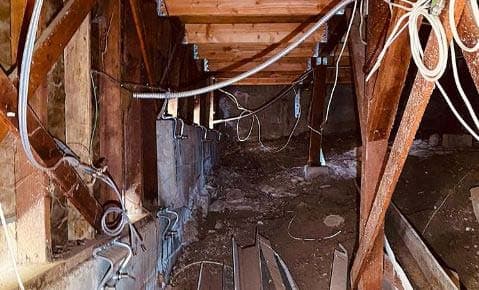 Crawl space under a raised home, with short timber cripple walls on the foundation and wiring along the framing