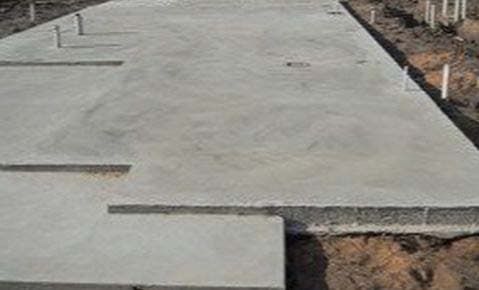 Newly poured concrete slab with plumbing stubs rising through it, on a residential lot