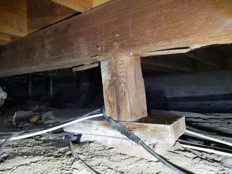 Wooden support post on a concrete pier block under a floor girder in a crawl space