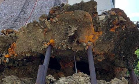 Steel piles exposed beneath a mass of soil and rock where a slope has eroded away