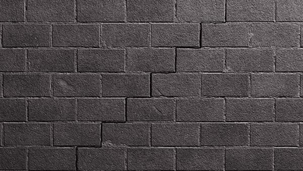 Stair step crack running through the mortar joints of a dark concrete block wall