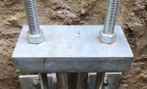Steel bracket with two threaded rods and nuts bolted to a pier in an excavation
