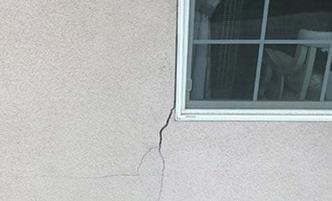 Crack spreading down a stucco wall from the corner of a window
