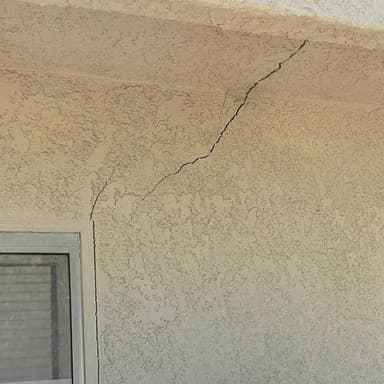 A crack in exterior stucco running from the top corner of a window up toward the eave