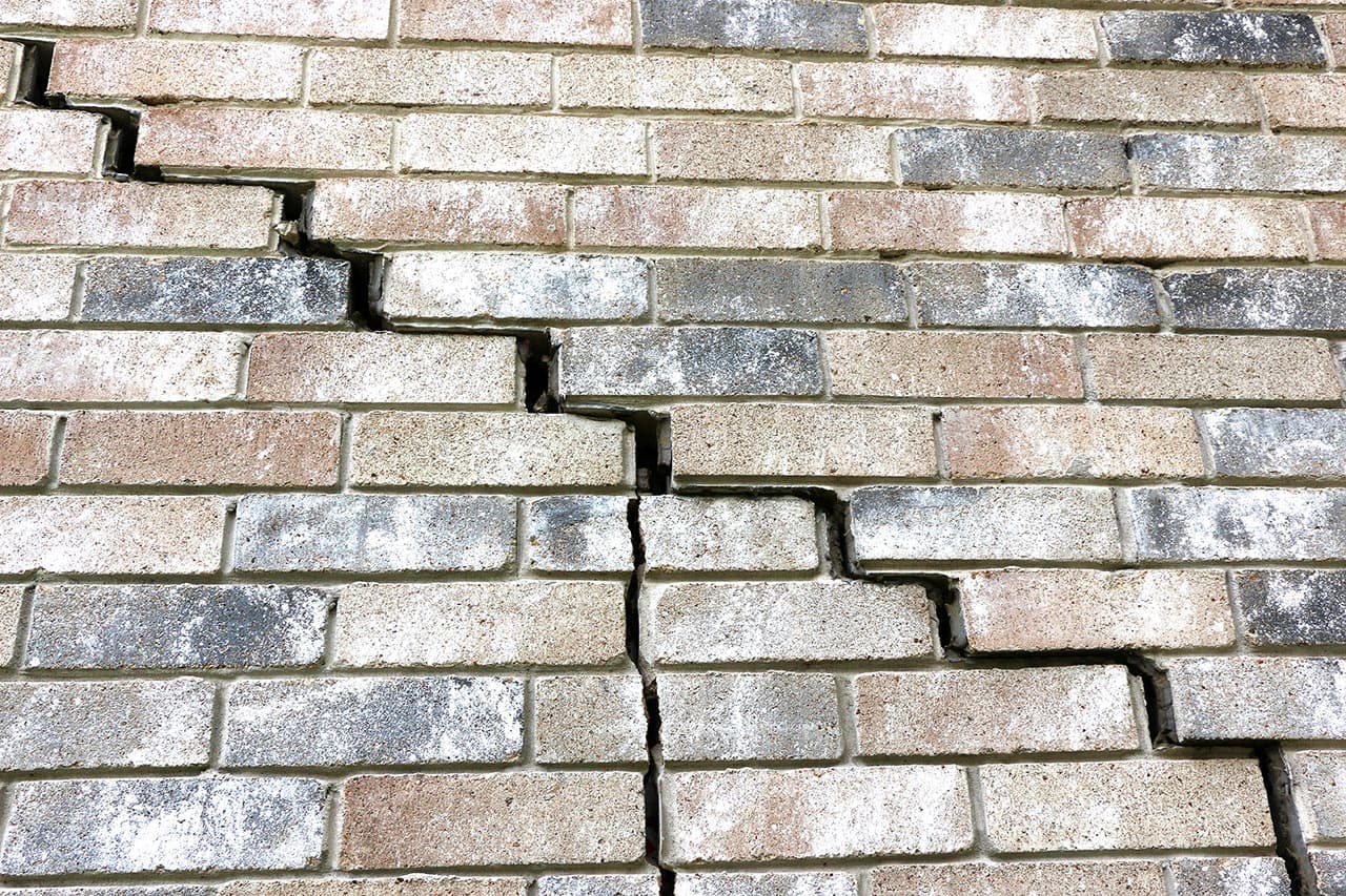 Dalinghaus Foundation Repair inspecting a severe stair-step crack in an exterior brick foundation wall.