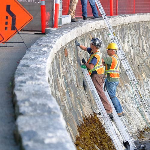 Dalinghaus Foundation Repair technicians on ladders inspecting and repairing a curved stone seawall