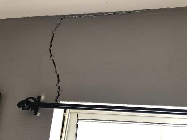 Dalinghaus Foundation Repair inspecting a severe vertical crack extending from the ceiling above a window, indicating structu
