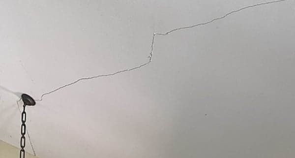 Dalinghaus Foundation Repair inspecting hairline cracks in a residential ceiling near a light fixture.