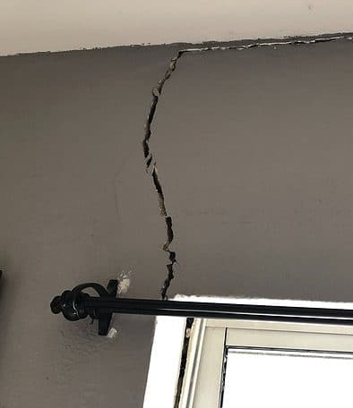Dalinghaus Foundation Repair inspecting a severe vertical crack in a gray interior wall, extending to the ceiling near a wind