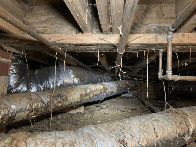 Dalinghaus Foundation Repair inspecting a dirty crawl space with sagging ductwork, exposed pipes and debris on the ground