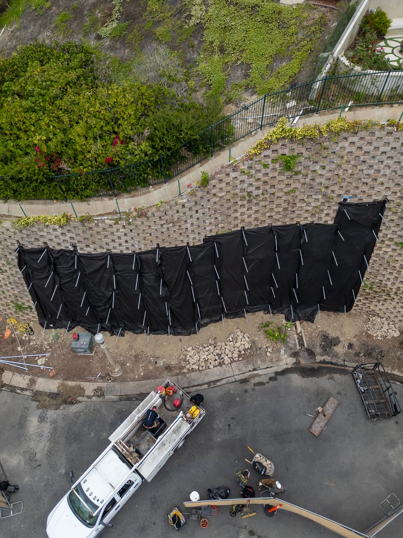 Dalinghaus Foundation Repair crew working on a leaning retaining wall with geotextile fabric and construction equipment.