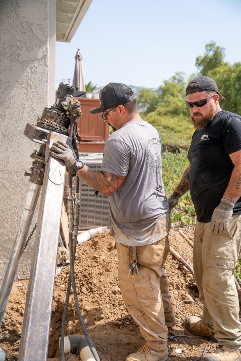 Dalinghaus Foundation Repair crew installing hydraulic push piers to stabilize a house foundation.
