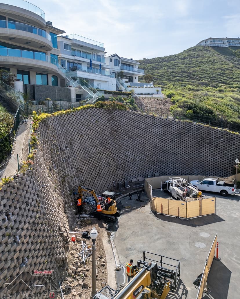 Dalinghaus Foundation Repair crew working with an excavator at the base of a large retaining wall on a hillside property.