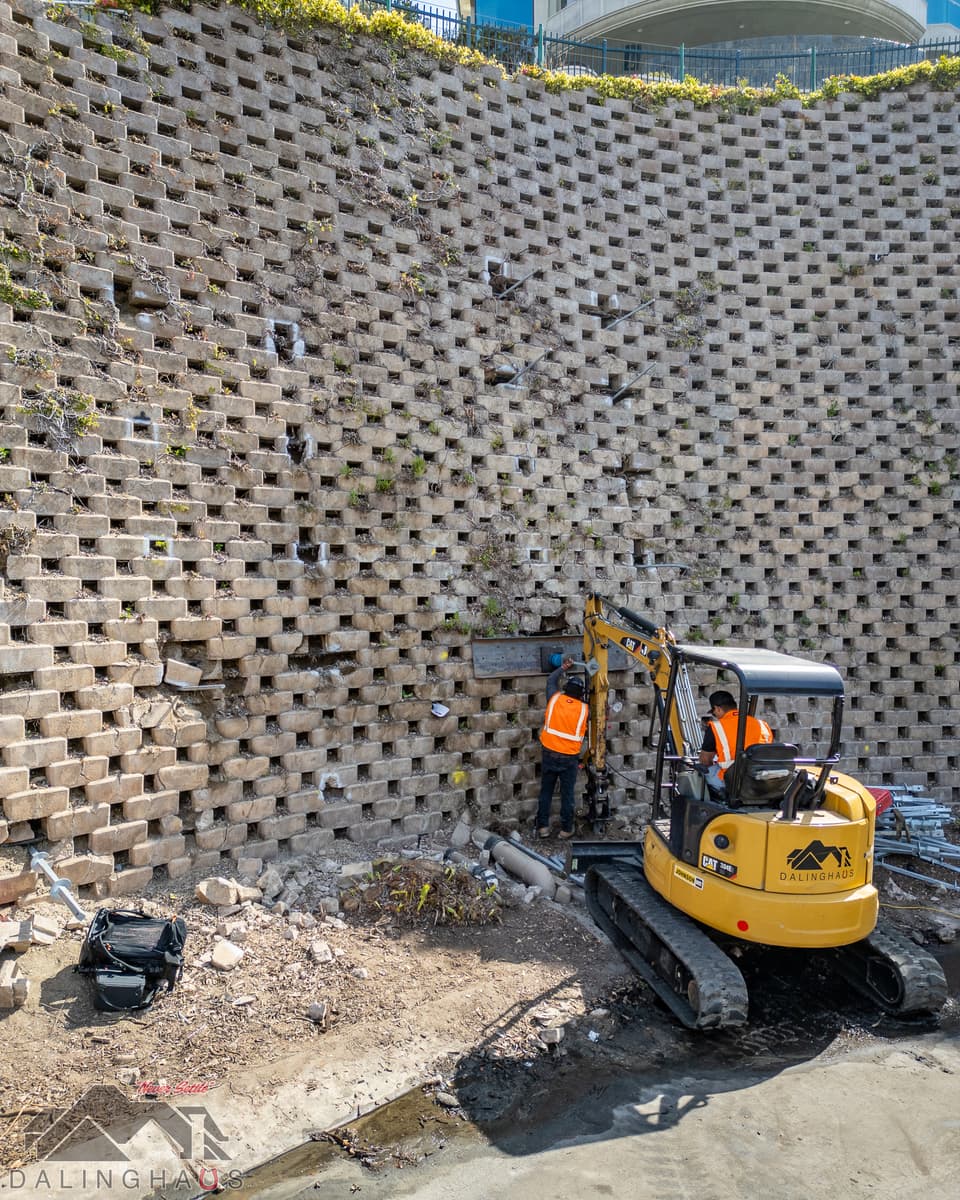 Dalinghaus Foundation Repair crew using a mini-excavator to install wall stabilization systems for a failing retaining wall.