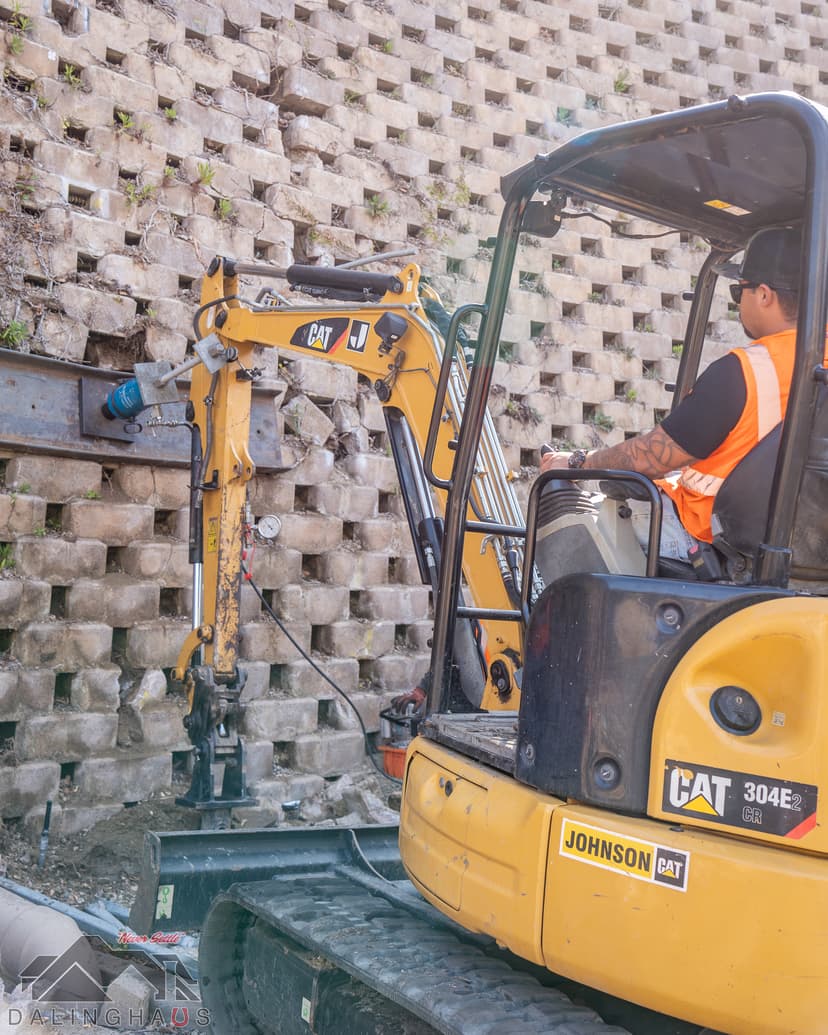 Dalinghaus Foundation Repair crew installing helical tieback anchors to stabilize a leaning retaining wall with an excavator.