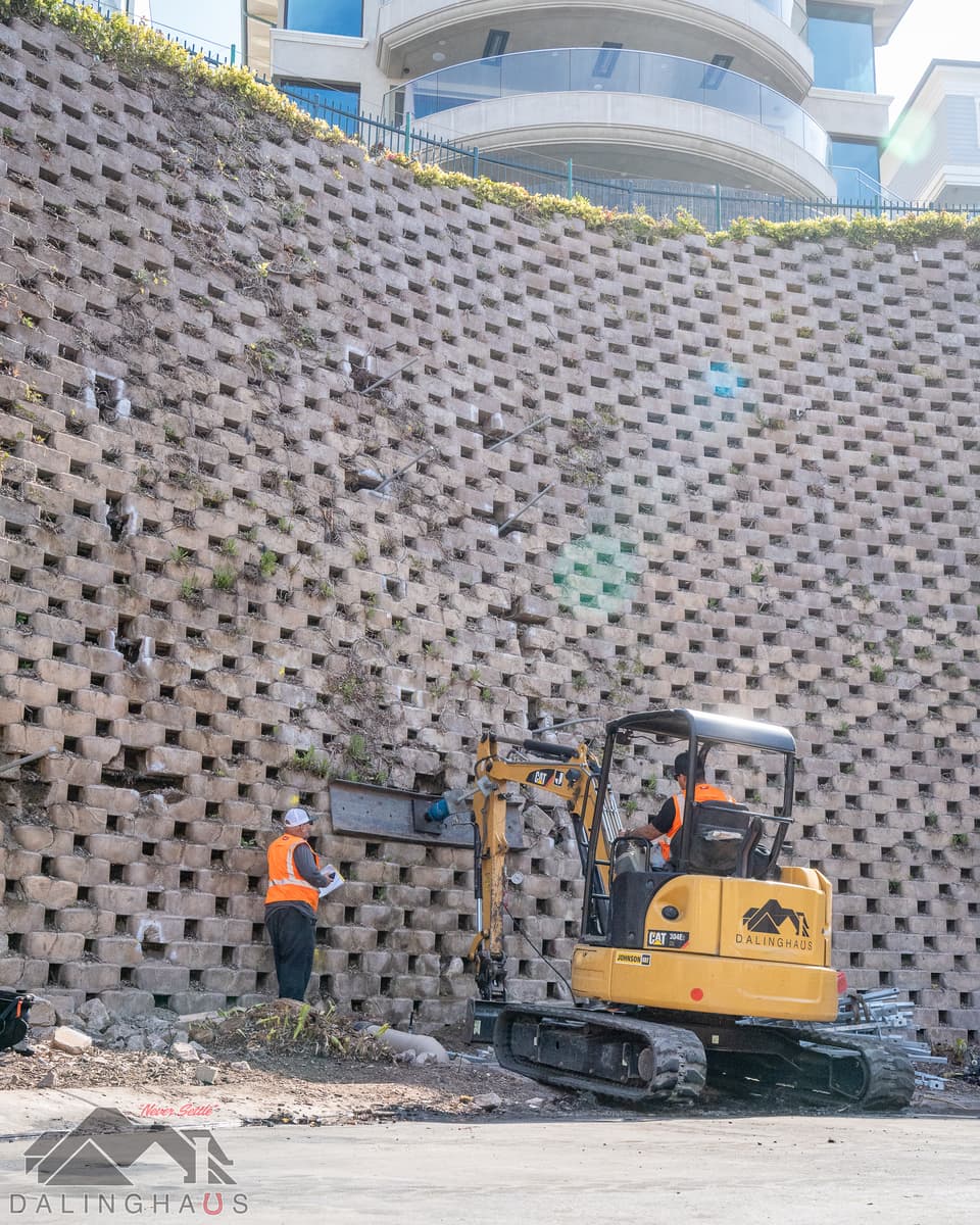 Dalinghaus Foundation Repair crew installing tieback anchors into a retaining wall, using a mini-excavator for structural