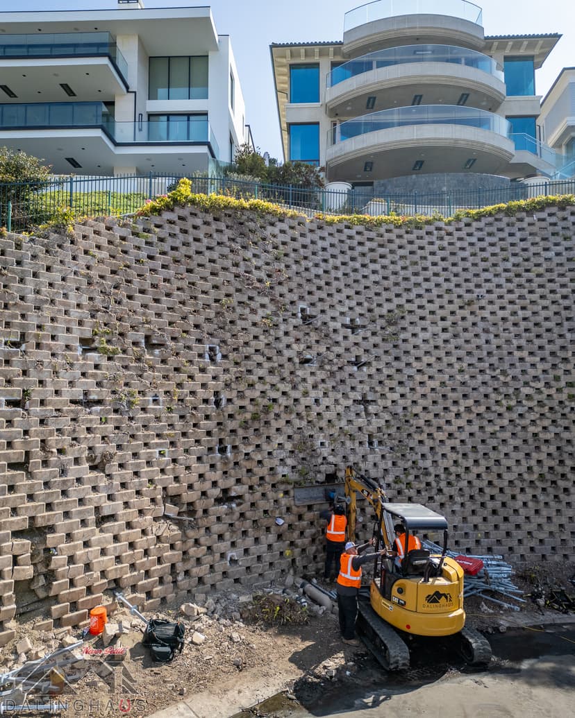 Dalinghaus Foundation Repair crew using an excavator to repair a large modular block retaining wall